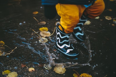 蹒跚学步的孩子穿着黑白雨靴站在水面上